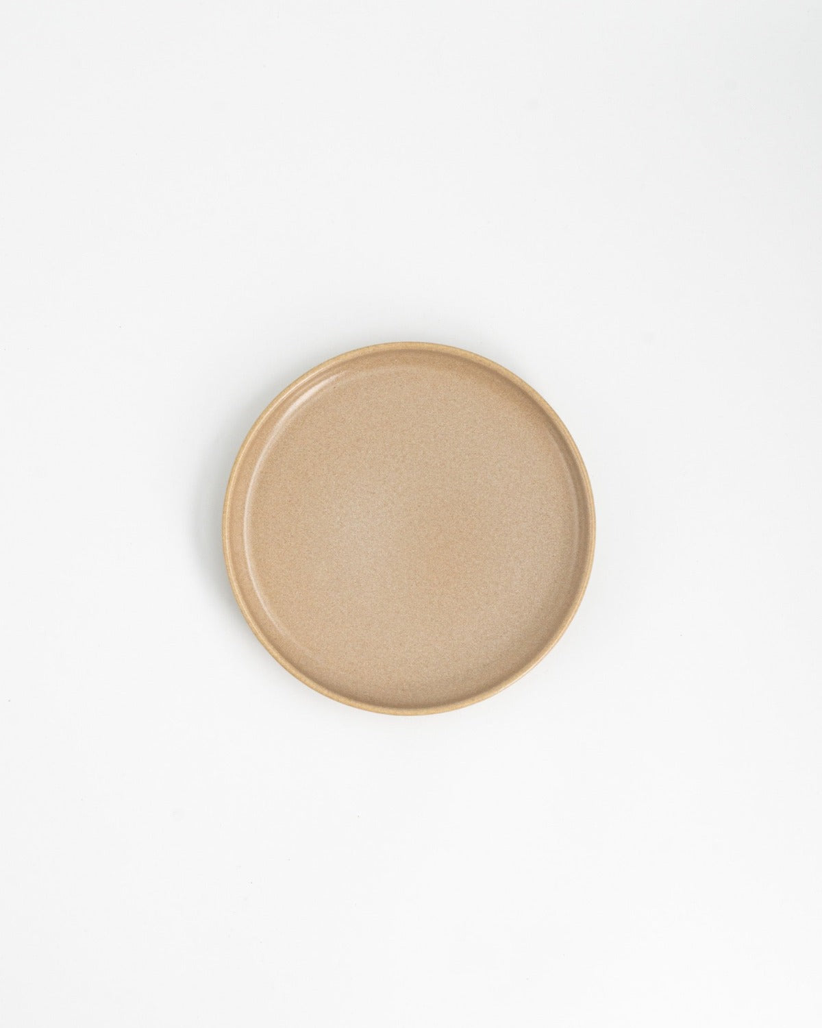 Beige tallrik i stengods fotograferad uppifrån mot en vit bakgrund