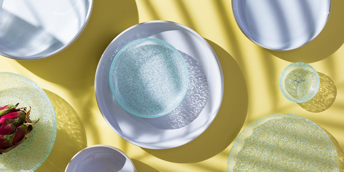 vita tallrikar i stengods och glas, uppdukade på ett bord med solgul duk